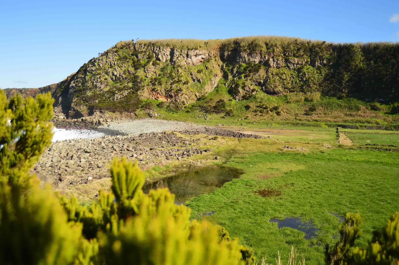 Baía de calhau rolado na costa da Agualva, com uma pequena lagoa e a falésia verde ao fundo