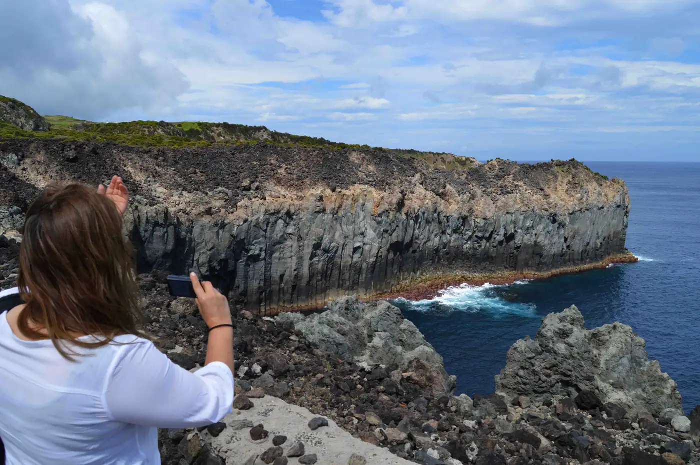 Caminhante a fotografar as falésias de basalto e o mar nas Baías da Agualva