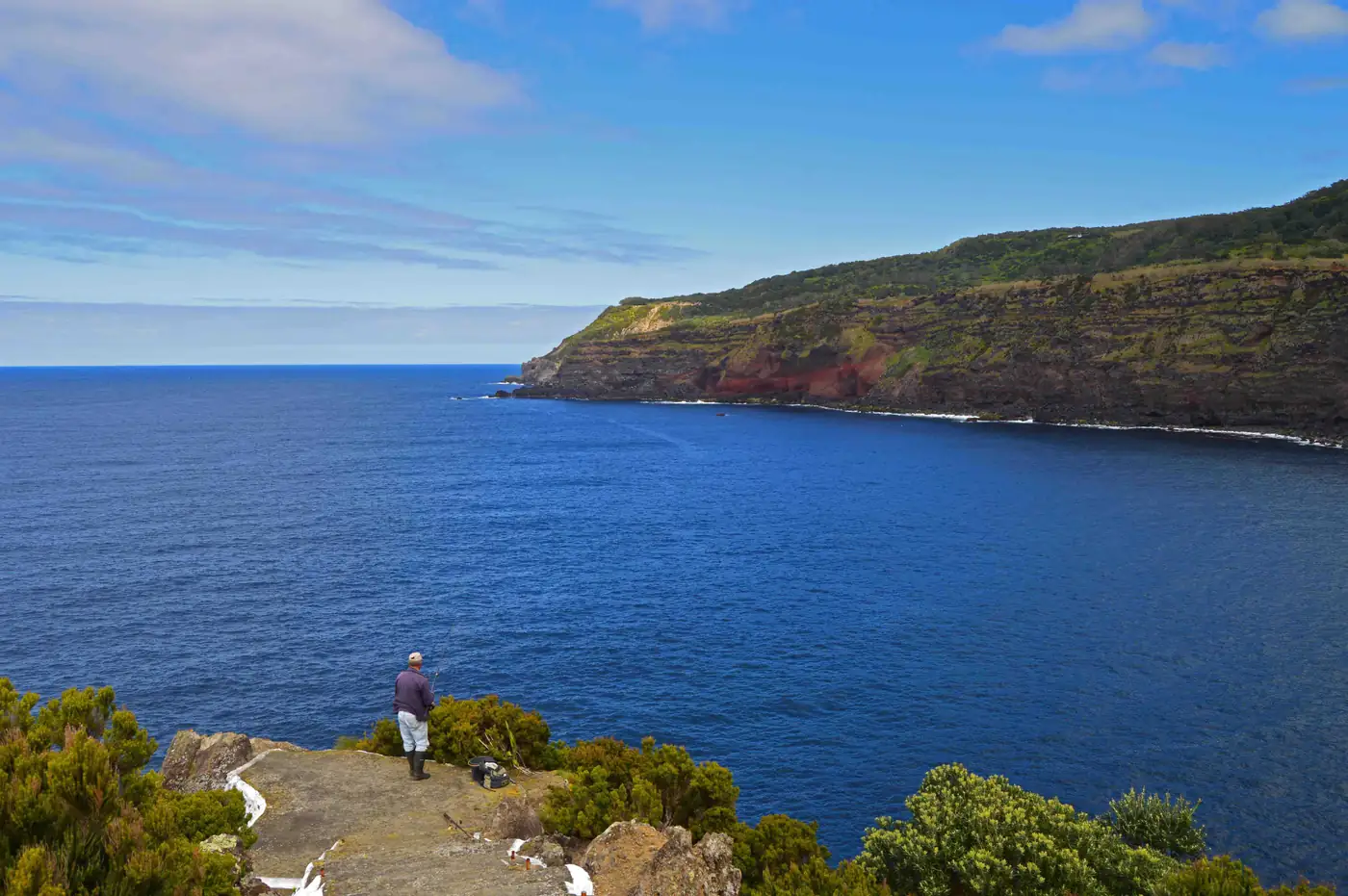 Visitante num miradouro sobre o mar azul, com a costa alta da Terceira ao fundo